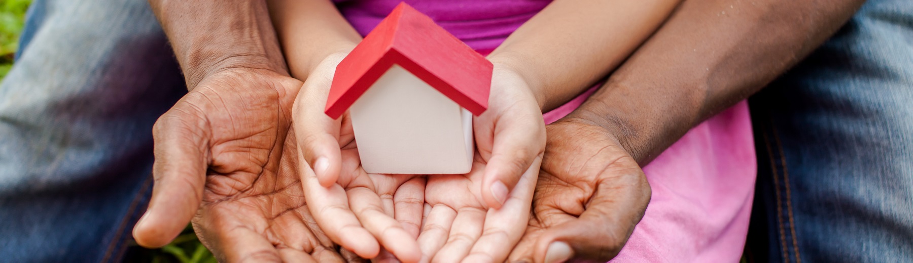 Image of a child holding a wooden house in their hands being supported by an adult's hands.