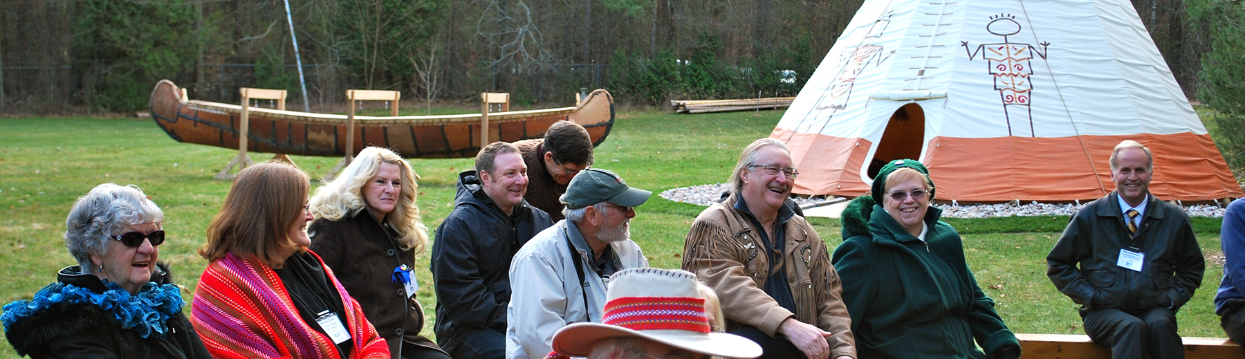 Canoe, teepee and people sitting on benches